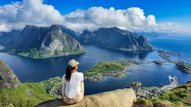 Kayalık bir çıkıntıda tek başına yürüyen bir yürüyüşçü gün doğumunda Lofoten Adaları 'nın büyüleyici fiyortlarına ve dağ zirvelerine hayran kalır. Şafağın parlak renkleri huzurlu manzarayı aydınlatır, macerayı artırır..