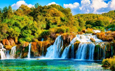 Büyüleyici Krka şelaleleri, Hırvatistan 'ın Krka Ulusal Parkı' ndaki sıcak bir yaz akşamında yemyeşil manzaralarda şelaleler boyunca akarak huzurlu bir atmosfer yaratıyor..