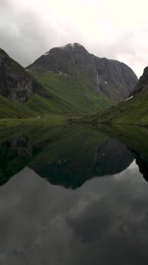 Huzurlu bir göl üzerindeki görkemli dağların kulesi gibi Norveç 'in dingin güzelliğini keşfedin. Mükemmel ayna benzeri bir yansıma oluşturun. Gri bulutlar bu sakin ortama mistik bir dokunuş ekler..