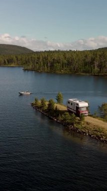 Huzurlu bir Norveç gölünün kenarında park edilmiş rahat bir karavanın görüntüsü. Çevreyi saran yemyeşil ormanlar ve görkemli dağlar açık hava maceralarını davet ediyor..