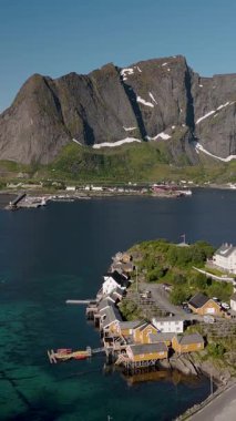 Norveç 'in büyüleyici bir kıyı köyünün nefes kesici manzarası, arka planda çarpıcı dağlar bulunan berrak mavi sularla çevrili. Sakrisoy, Moskenes, Lofoten adaları. Norveç.