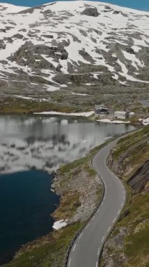 Resmedilmeye değer bir hava perspektifi Norveç 'te sakin bir gölün kenarını izleyen kıvrımlı bir yol sergiliyor. Etrafı görkemli dağlar ve kar parçalarıyla çevrili..