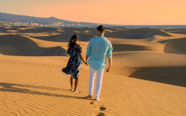 Bir erkek ve kadın el ele yürür Maspaloma 'nın altın kum tepelerinde, Gran Canaria' da. Sıcak akşam ışığı romantik bir parıltı yayar ve huzurlu bir tatil anı yaratır..