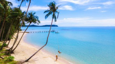 İki Taylandlı kadın ve Avrupalı erkek Koh Kood, Tayland 'da güzel bir plajda dinleniyorlar. Palmiye ağaçlarının altında neşeli bir şekilde sallanırlar, berrak mavi suları ve sakin bir atmosferi vardır, tropikal kaçışlar için mükemmeldir..