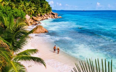 Genç bir çift el ele gezer Anse Patates 'in el değmemiş kumları boyunca, yemyeşil palmiye ağaçları ve La Digue Seyşeller' in canlı mavi sularıyla çevrili..