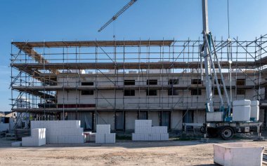 Hollanda 'daki canlı bir inşaat sahasında yeni inşa edilen aile evleri sergileniyor. İşçiler modern evler inşa etmekle meşguller. İskeleler ve makineler kullanarak varoşları hoş karşılayan bir mahalle oluşturuyorlar..