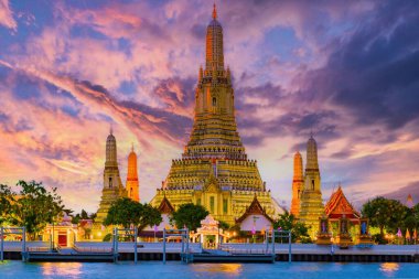 Altın renkler Wat Arun tapınağını aydınlatıyor güneş Bangkok 'ta batarken. Görkemli yapı, Chao Phraya Nehri 'nin etrafındaki sularda huzuru yansıtan canlı bir gökyüzüne karşı duruyor..