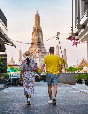 Akşam yaklaşırken, bir çift Bangkok 'ta büyüleyici bir cadde boyunca el ele yürür, gün batımının sıcak renkleriyle aydınlanan ve nefes kesici Wat Arun' a doğru yol alırlar..