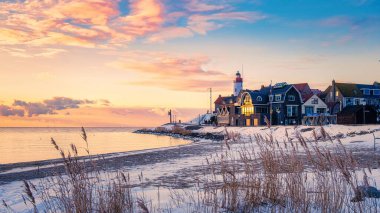 Hollanda 'da sakin bir plajda güneş batarken, renkli evler altın renkleri yansıtıyor. Yumuşak dalgalar kumlu sahili öper ve kışın Urk fenerinde huzurlu bir atmosfer yaratır.