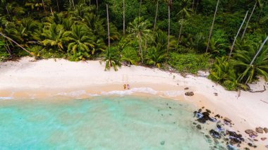 Tayland 'da altın saat boyunca, bereketli palmiye ağaçları ve berrak turkuaz sularla çevrili sakin bir sahil boyunca el ele dolaşırlar. Sakin atmosfer romantizmi çağrıştırıyor. 