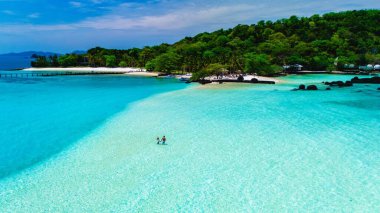 Kristal berraklığında turkuaz sularla çevrili el değmemiş beyaz kumların üzerinde duran iki insan. Koh Mak Tayland yakınlarındaki Koh Kham Adası.