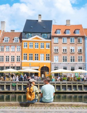 Bir çift, Danimarka 'da Nyhavn, Kopenhag' da renkli binalar ve hareketli kafelerle çevrili güzel bir Danimarka kasabasında liman kenarında sakin bir anın tadını çıkarıyor.