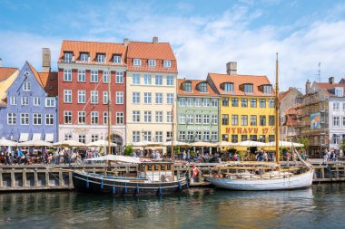 Kopenhag, Danimarka, 12 Temmuz 20204, renkli cepheler ve açık hava kafeleriyle dolu canlı binalar, Nyhavn rıhtımında. Ziyaretçiler güneşin tadını çıkarırken kayıklar suda hafifçe sallanır.