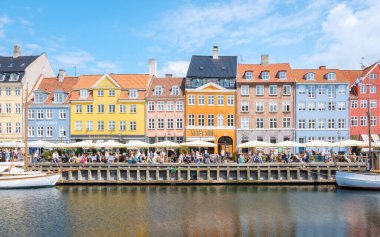 Nyhavn, Kopenhag, Danimarka, 12 Temmuz 204: Neşe dolu kafeler ve canlı atmosferin tadını çıkaran ziyaretçilerle dolu rıhtım. Ayar güneşli bir günün cazibesini yansıtıyor. 