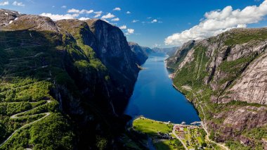 Görkemli fiyortlar, yemyeşil yemyeşil ve durgun suların masmavi gökyüzünü yansıttığı yüksek uçurumlar arasında uzanıyor. Bu sakin manzara saf güzelliği ve ihtişamı sergiliyor. Lysefjord, Norveç, 