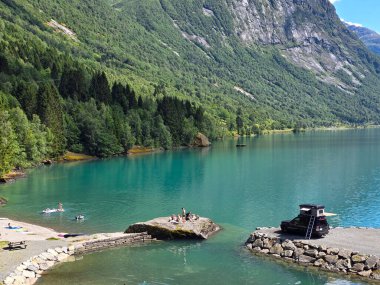 Lovatnet Loen 26 Haziran 2024, Norveç, Ziyaretçiler göz kamaştırıcı Norveç dağlarıyla çevrili güneşli bir gölde huzurlu bir yaz gününün tadını çıkarıyorlar.. 