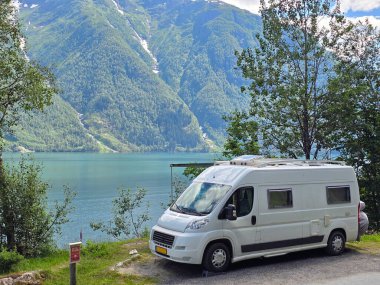 Norveç fiyortlarının sakin kıyılarına park edilmiş nefes kesen dağlarla çevrili pitoresk bir karavan. Canlı yeşillik ve berrak mavi su cennet gibi bir açık hava kaçışı yaratır..