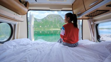 Bir kadın, rahat bir karavanda, nefes kesen dağlara ve Norveç 'te sakin bir su kütlesine bakan bir huzur anının tadını çıkarıyor. Barışçıl atmosfer keşfi davet ediyor.