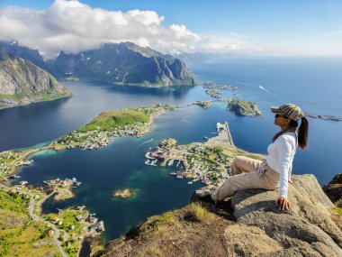 Bir gezgin Norveç 'teki Lofoten Adaları' nın büyüleyici manzarasına bakan kayalık bir çıkıntıda oturur..