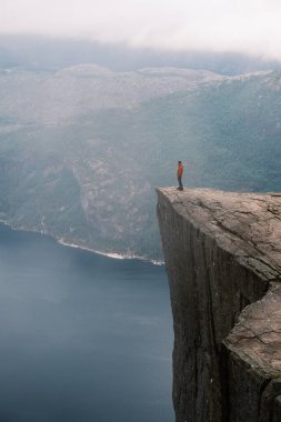 Preikestolen 'in kıyısında bir heyecan arayıcısı duruyor, aynı zamanda Pulpit Rock olarak da bilinir, Norveç' teki büyüleyici Lysefjord 'a tepeden bakan. Manzaralı manzaralar ve dramatik uçurumlar unutulmaz bir deneyim yaratır..
