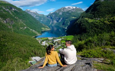 Bir çift, Geiranger Norveç 'in çarpıcı fiyort manzarasına hayran kalarak kayalık bir çıkıntıda oturuyor..