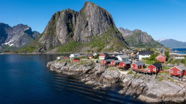 Norveç 'in pitoresk bir kıyı köyü, yüksek bir dağ zeminine karşı canlı kırmızı kulübeler sergiliyor. Hamnoy, Lofoten 'daki balıkçı köyü.