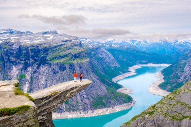 İki maceracı ikonik Trolltunga 'da duruyor, Norveç kaya oluşumunda, aşağıdaki Lysefjord' un nefes kesici manzarasını izliyorlar..