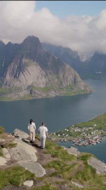 Bir çift, görkemli dağlar ve sakin sularla çevrili Reinebringen Lofoten Norveç 'in engebeli kıyı şeridi boyunca manzaralı bir yürüyüşün tadını çıkarıyor. Sakin fiyort doğanın güzelliğini yansıtır..