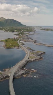 Norveç 'in yemyeşil manzaralarının arkaplanına uzanan dolambaçlı bir kıyı otoyolunun nefes kesici manzarası. Turkuaz sular engebeli kıyı şeridini nazikçe kucaklıyor ve sakin bir kaçış yaratıyor..