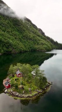 Huzurlu bir fiyortta, yemyeşil ve dingin sularla çevrili bir adada büyüleyici kırmızı kulübeler duruyor. Bu cennet manzarası bulutlu havada Norveç 'in doğal güzelliklerini gözler önüne seriyor..