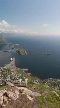 Resimli adaları ve engebeli dağları gözler önüne seren Lofoten Norveç 'in göz kamaştırıcı manzaralarının tadını çıkarın. Yürüyüşçüler, güneşli bir günde, sakin manzarayı ve berrak mavi suları alan bir zirvenin tepesinde dururlar..