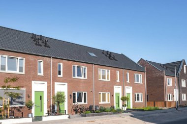 Çağdaş tuğladan evler sakin bir caddeyi kaplıyor ve Hollanda 'da açık mavi gökyüzü altında eşsiz girişlerini ve zevkli manzaralarını sergiliyor.