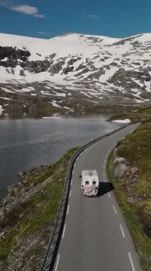 Heybetli dağlar, dingin bir fiyordu saran dolambaçlı bir yolun yanında yükselir. Bir karavan, Norveç 'in doğal güzelliklerini gösteren, manzarayı aydınlatan bu manzarada seyahat eder..