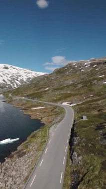 Etkileyici karlı dağlarla çevrili sakin bir gölün hatlarını takip eden dolambaçlı bir yolun nefes kesici manzarası..