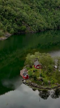 İki büyüleyici kırmızı kulübe yemyeşil ve sakin fiyortlarla çevrili küçük bir adada huzur içinde oturuyor. Norveç 'in el değmemiş güzelliği, Lovrafjorden, Norveç' te huzurlu bir kaçış yaratır.