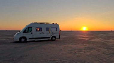 Güneş ufukta batarken, Romo Lakolk Sahili 'nin geniş kumlarında rahat bir karavan duruyor. Huzurlu atmosfer, doğayla bağ kurmak ve gevşemek için mükemmel bir kaçış sağlar..