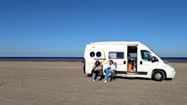Danimarka 'nın Romo Lakolk plajında huzurlu bir gün başlıyor. İki kişi karavanın önünde dinleniyor. Bir kaç erkek ve kadın tatilde.
