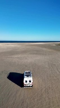 Danimarka 'nın Romo kentindeki Lakolk Sahili' nin engin ve sakin manzaralarını keşfedin. Yalnız bir araç, temiz mavi bir gökyüzünün altında el değmemiş kumlu kıyılarda dolaşır..