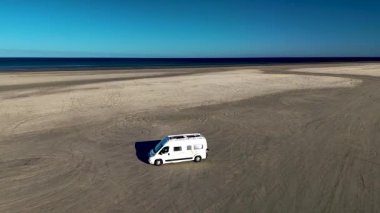 Danimarka 'da Romo Lakolk plajı boyunca uzanan geniş kumsalda, açık mavi gökyüzünün altında bir karavan bulunur. Güzel kıyı manzarası dinlenmek için sakin bir atmosfer yaratıyor..