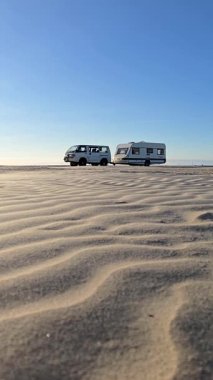 Danimarka 'daki Romo Lakolk plajında huzurlu bir günün tadını çıkarın. İki minibüs yumuşak, kumlu sahilde dinleniyor..