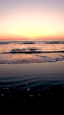 Güneş, Danimarka 'nın Romo Lakolk plajında batarken kumlu kıyıya yumuşak dalgalar vuruyor. Renkli gökyüzü suya çok güzel yansıyor. Rahatlamak için mükemmel sakin bir atmosfer yaratıyor..