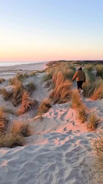 Bir gezgin, Romo Lakolk plajının yumuşak kumlu kumları boyunca otlar ve günbatımının ılık renkleriyle birlikte yürüyor. Sakin atmosfer keşif ve rahatlamaya davetiye çıkarıyor..