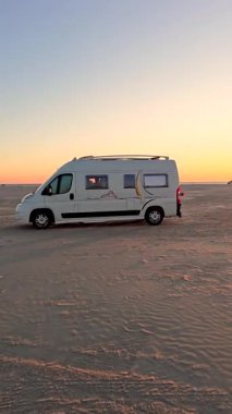 Danimarka 'nın Romo Lakolk plajındaki sakin atmosferi bir karavanın çarpıcı bir günbatımına doğru parkedişini izleyin. Yumuşak kumlar, altın ışık ve geniş gökyüzü huzurlu bir kaçış yaratır..