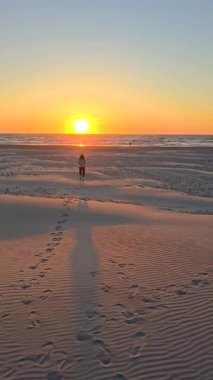 Günbatımının altın renkleri Danimarka 'nın Jutland kentindeki sakin Lakolk plajını aydınlatır. Yalnız bir kadın kumlu sahil boyunca yürüyor, yumuşak kumda ayak izleri bırakıyor dalgalar yavaşça kıyıya vururken.