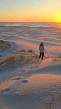 Huzurlu bir gezgin, altın saat boyunca Lakolk sahilinin yumuşak kum tepelerini keşfeder. Huzurlu ortam, güneş ufkun altına batarken dalgaların yavaşça kıyıya vuruşunu gösteriyor..