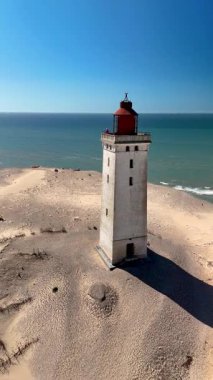 Kuzey Denizi 'nin sakin mavi sularıyla çevrili Rubjerg Knude Fyr, Jutland, Danimarka' nın kumlu kıyılarında gururla duran görkemli bir deniz feneri berrak bir gökyüzünün altında..