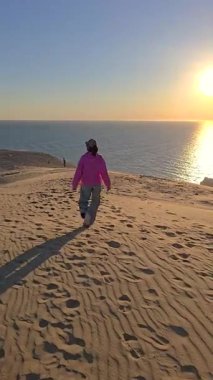 Güneş sakin denizin üzerinde batarken, Danimarka 'nın Rubjerg Knude Jutland kentinin geniş kumullarında sakin bir şekilde yürüyen bir insan manzarada sıcak altın bir parıltı yayar..