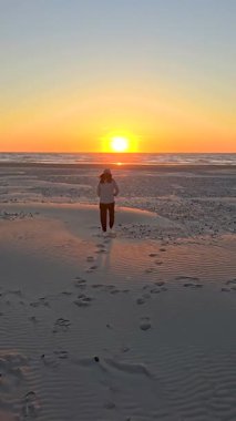 Altın güneş ışığı Lakolk sahilinde kıyıda yürürken Jutland Danimarka 'daki kumlu plajın izini sürüyor. Sakin atmosfer, gün batımında Jutlands 'ın dingin güzelliğini vurgular..