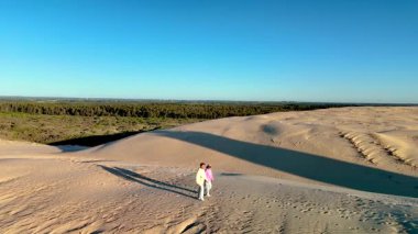 Çift, Danimarka 'nın Jutland kentindeki Rubjerg Knude Fyr Deniz Feneri' nin güzel kumlu arazisinde geziniyor. Altın tepeler ve berrak mavi gökyüzü sakin bir atmosfer yaratır.