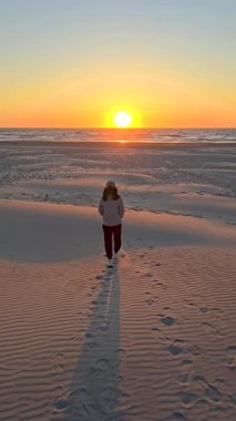 Danimarka 'nın Jutland kentindeki Lakolk plajında huzurlu bir gezinti, canlı günbatımı kum tepelerinin üzerine sıcak renkler döküyor. Deniz kenarında dinlenen sakin bir an..